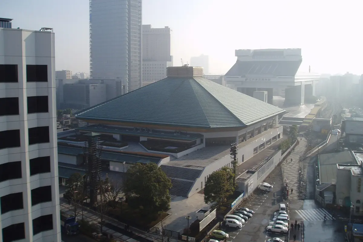 The green pyramid-shaped roof of the Ryogoku Kokugikan sumo hall in Tokyo, with the Edo-Tokyo Museum building behind it